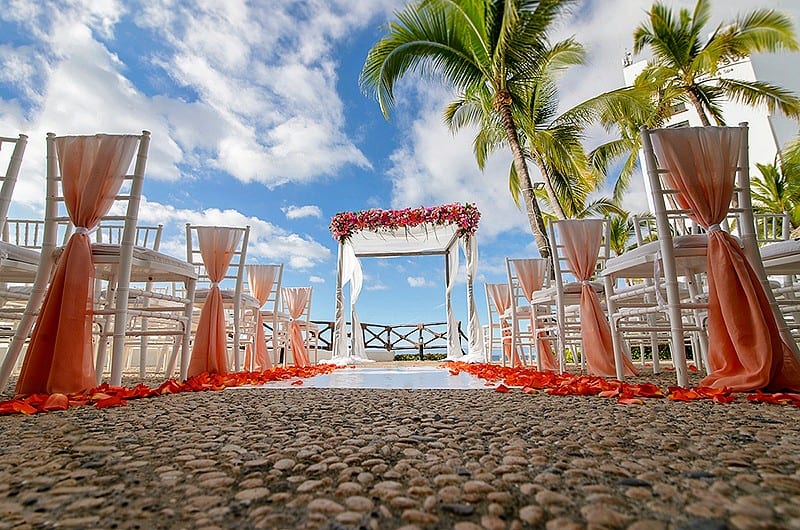 An outdoor wedding ceremony featuring rows of chairs adorned with flowers, set against a natural backdrop.