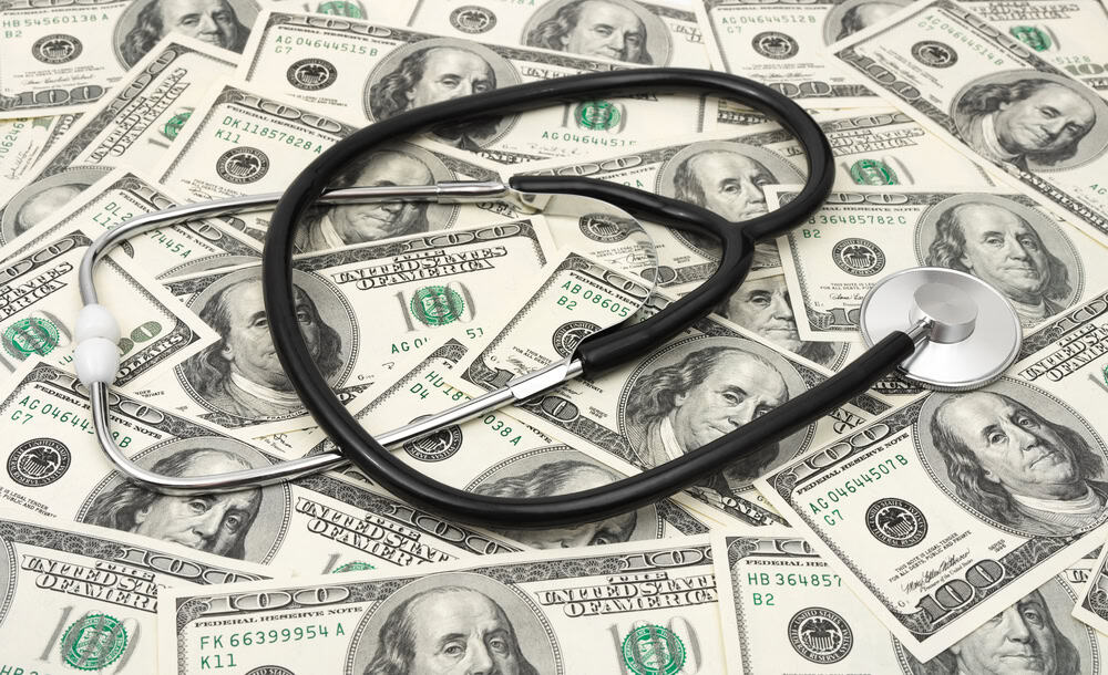 Stethoscope on scattered $100 bills representing police funding and healthcare.