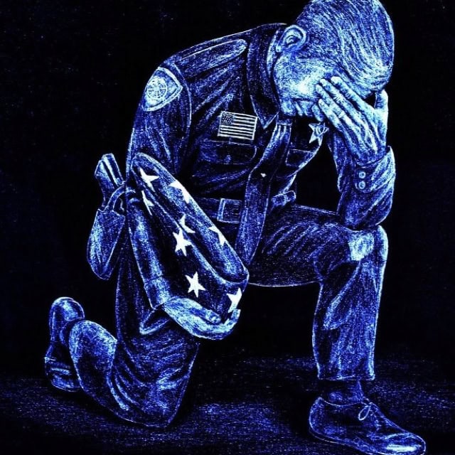 Police officer kneeling with American flag badge, showing distress and dedication.