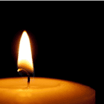 Close-up of a lit candle flame in darkness, symbolizing remembrance and hope.