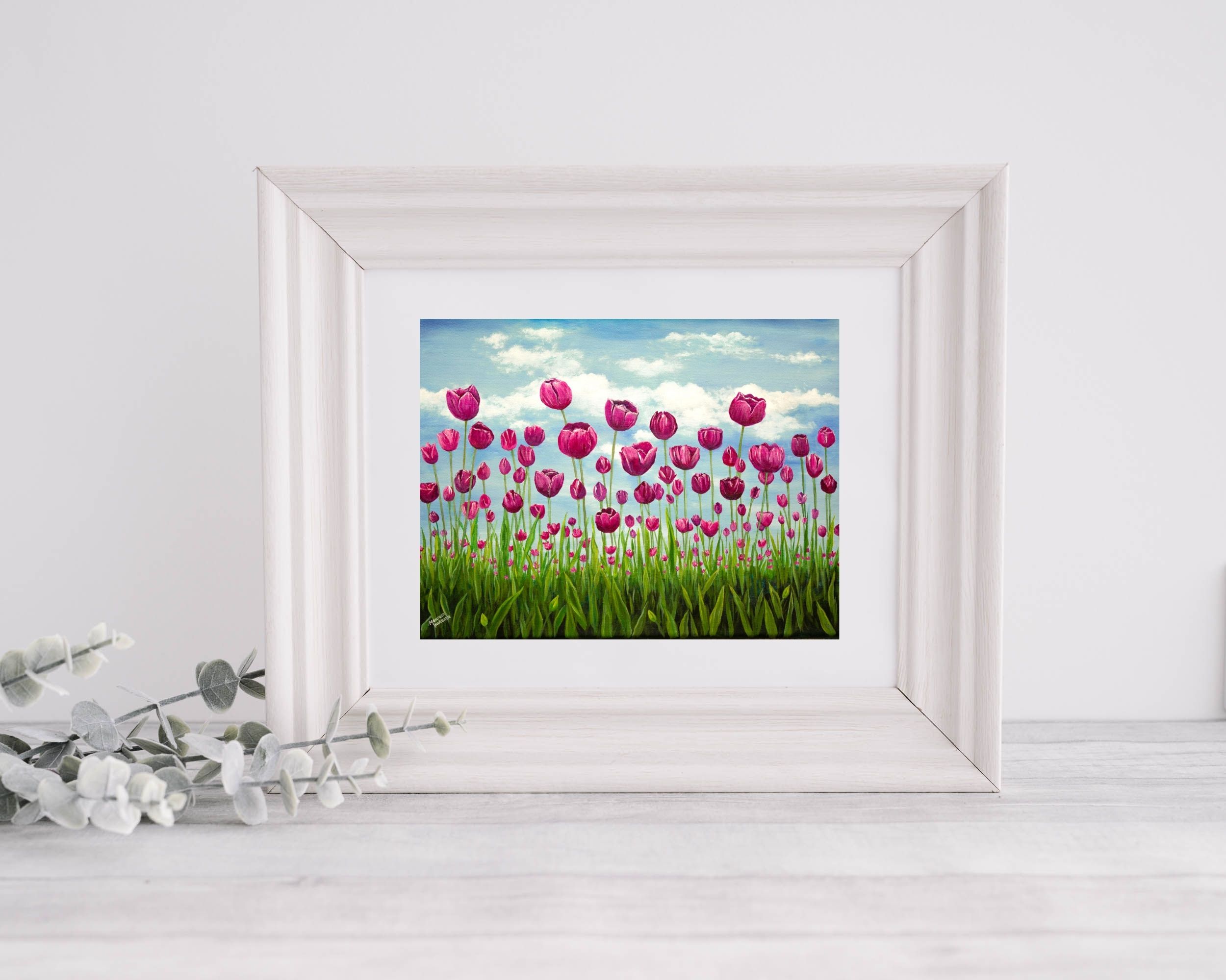 a giclee print of a field of pink vibrant tulips standing tall in a green field. The sky behind them is soft blue with fluffy clouds