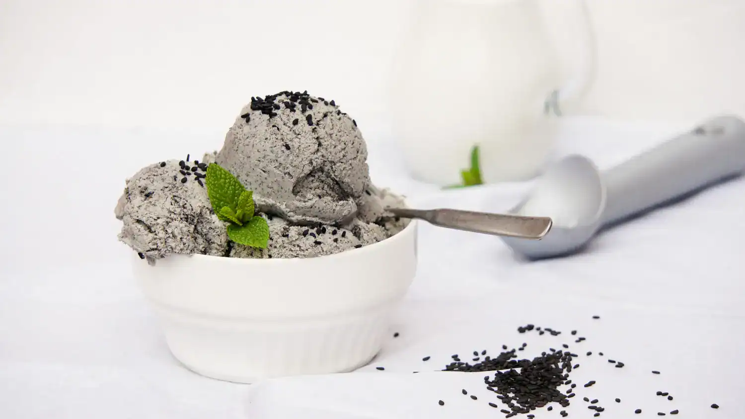 Black sesame ice cream scoop in a white bowl with mint garnish.