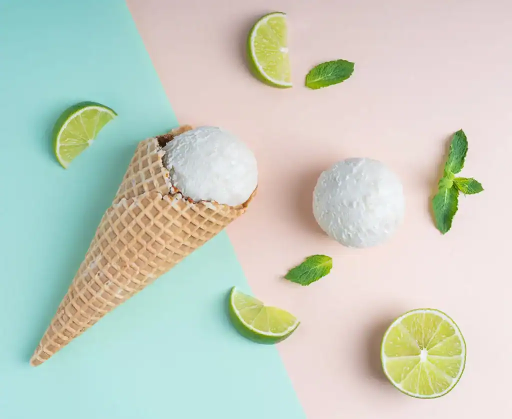 Delicious low-calorie coconut lime ice cream in a waffle cone with fresh lime wedges and mint leaves.