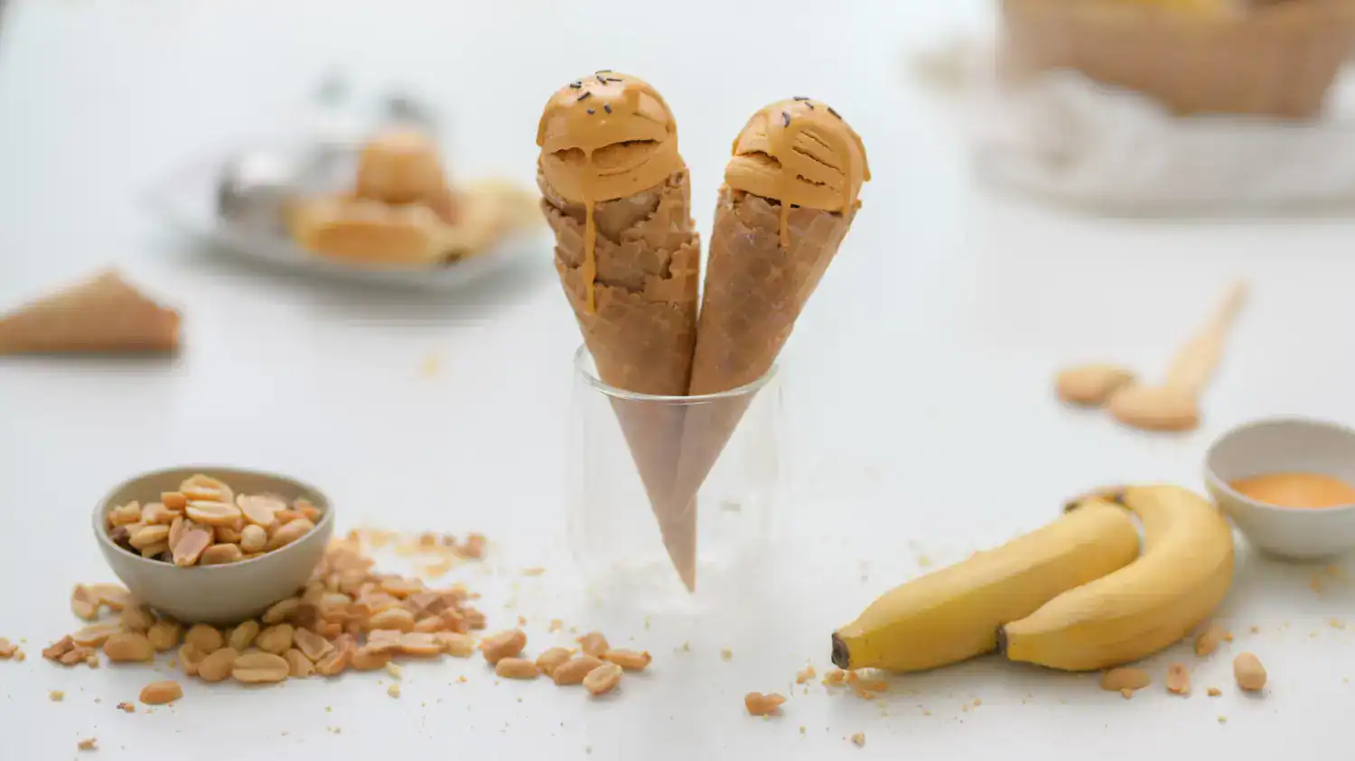 Delicious peanut butter banana ice cream cones served in a glass with bananas and toppings.