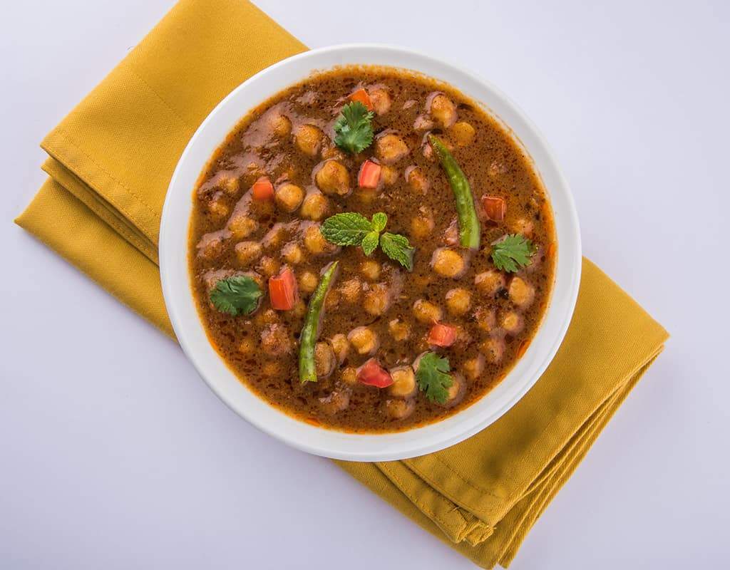 Spicy chickpea curry served in a white bowl with fresh herbs, on a yellow napkin.
