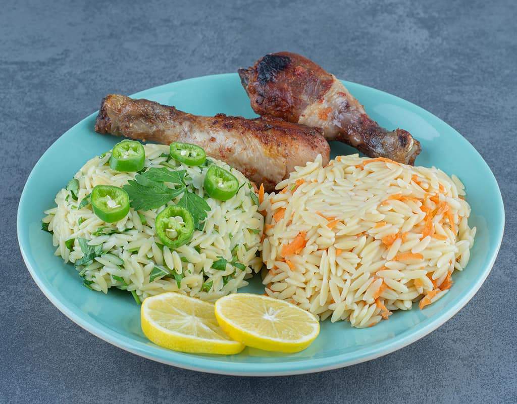 Spicy grilled chicken drumsticks with flavored rice and mint-topped orzo salad, served with lemon wedges.
