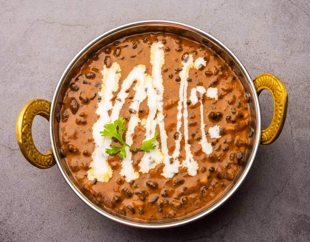 Spicy Indian lentil dal curry served in a traditional metal bowl with garnished cream and cilantro.
