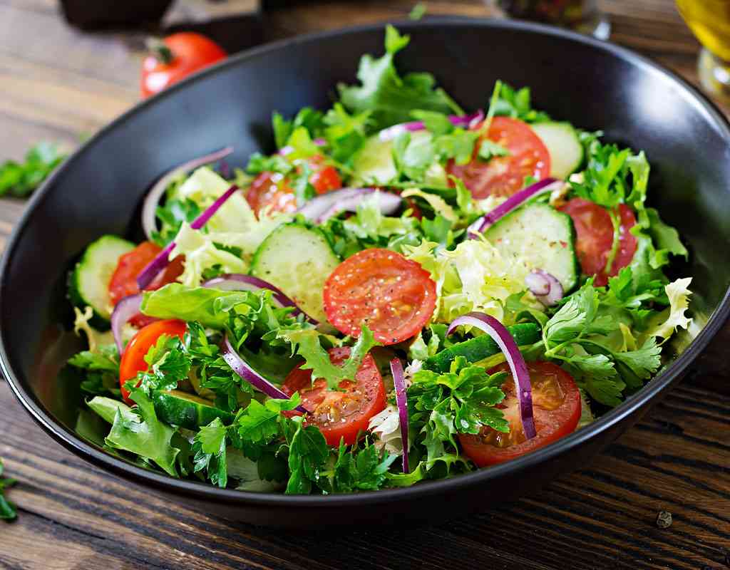Fresh Indian-style mixed salad with tomatoes, cucumbers, lettuce, and red onions in a black bowl.