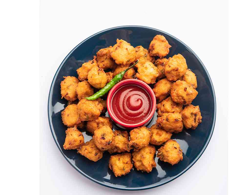 Crispy Indian chicken nuggets with spicy sauce and green chili on a dark plate.