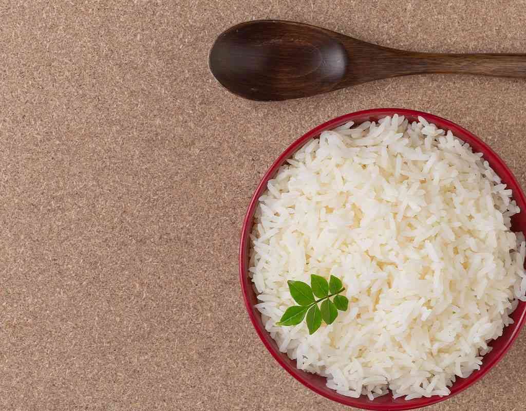 Steamed white rice with fresh herbs on a red bowl, perfect for Indian cuisine meals.