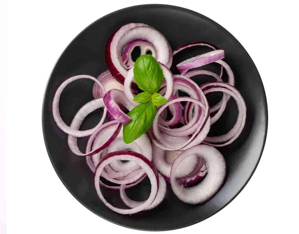 Fresh sliced red onions with basil on a black bowl, perfect for Indian cuisine dishes.
