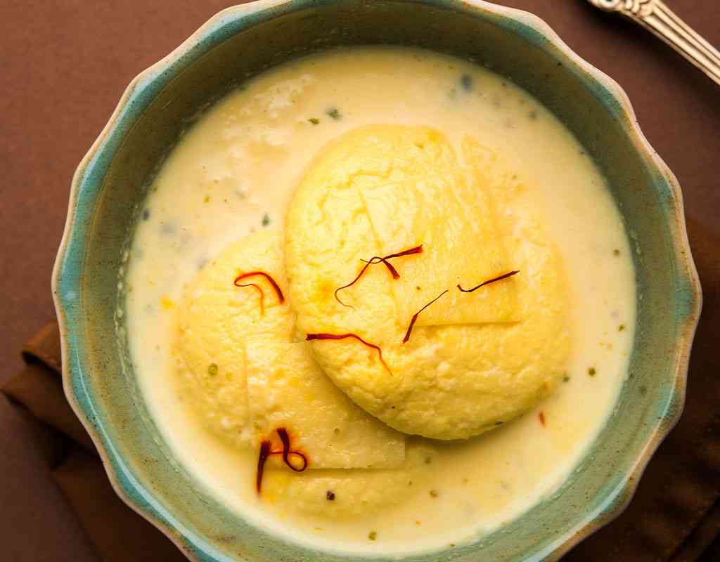 Rich Indian Ras Malai dessert with saffron threads, saffron syrup, and creamy milk in a ceramic bowl.