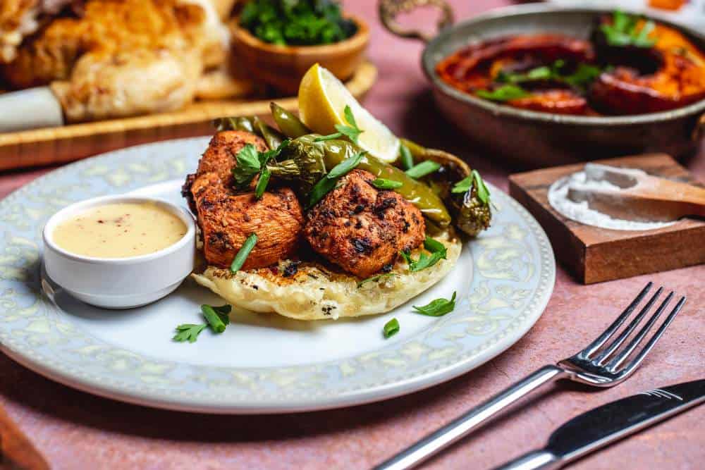 Succulent grilled chicken tikka served with naan, green chili peppers, and fresh lemon wedges.