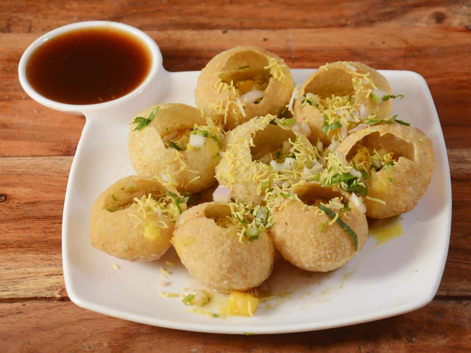 Crispy Indian pani puri with spiced water on white plate, traditional Mumbai street food.