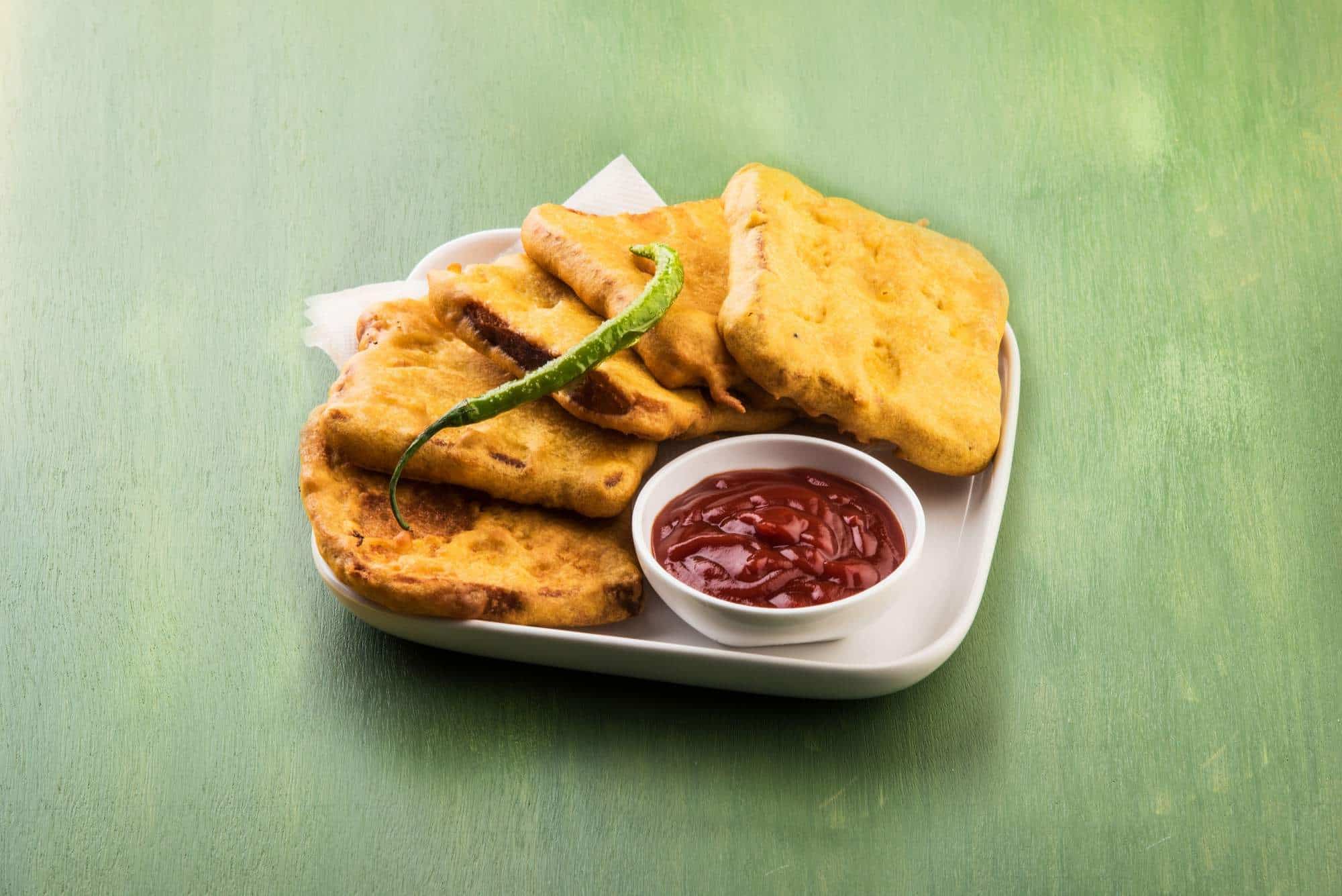 Crispy Indian snack platter with dipping sauce and green chili on a white plate.