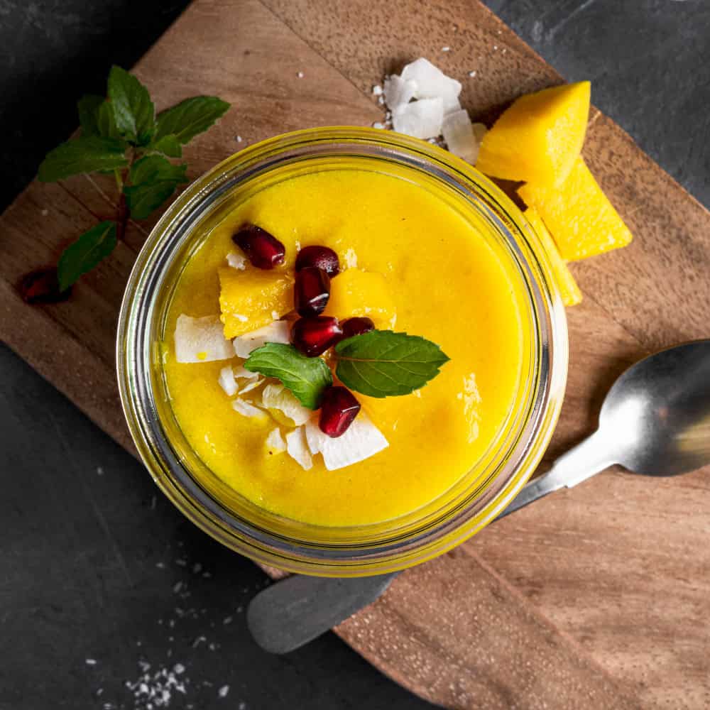 Mango lassi drink in a glass jar with mango pieces and garnishes, traditional Indian beverage.