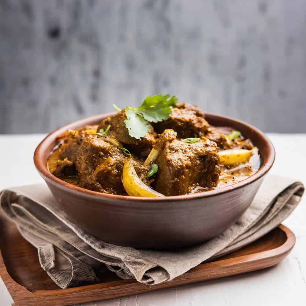 Spicy Indian lamb curry served in a brown bowl with herbs and onions, highlighting authentic Indian cuisine.