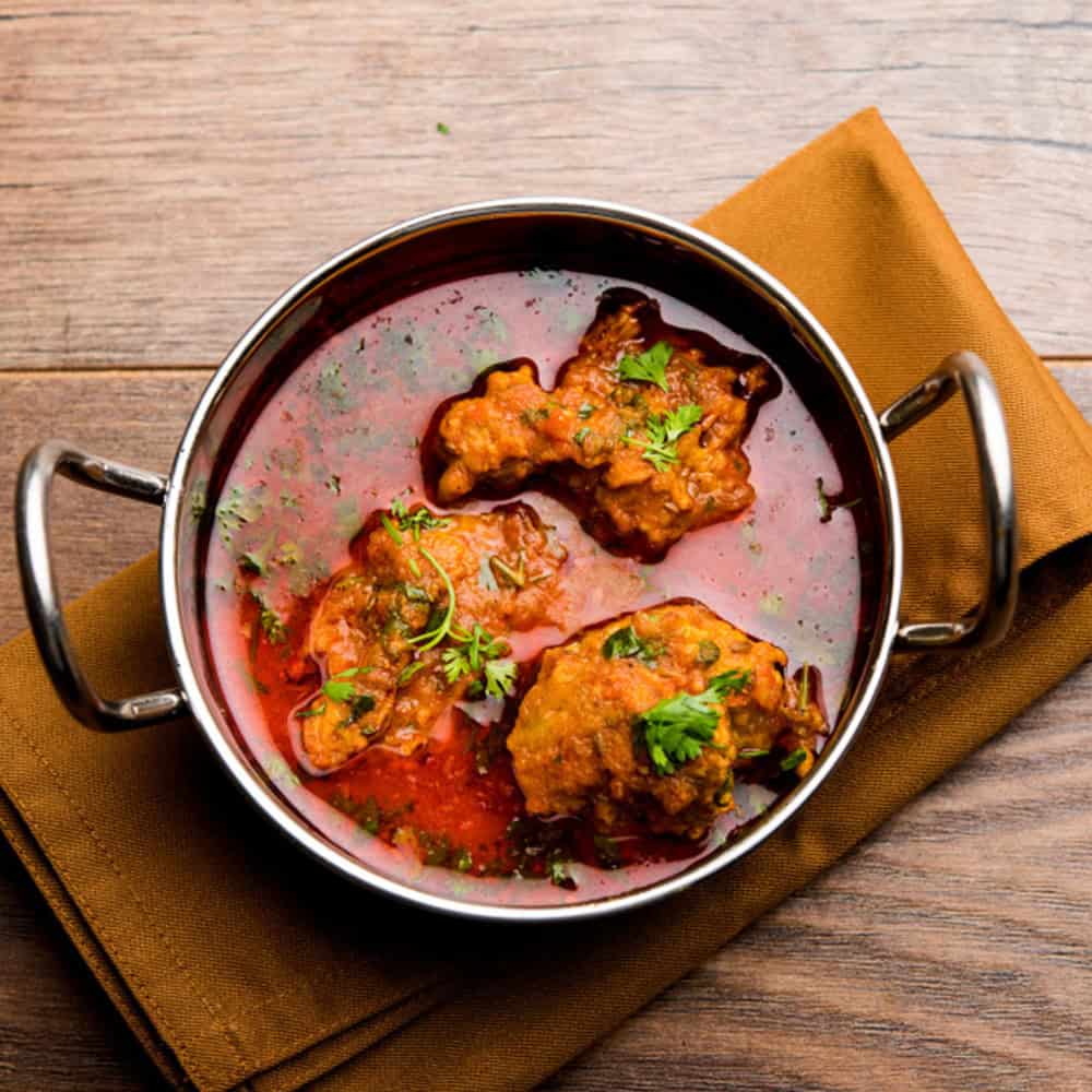 Spicy Indian chicken curry in a stainless steel bowl, served with fresh herbs.