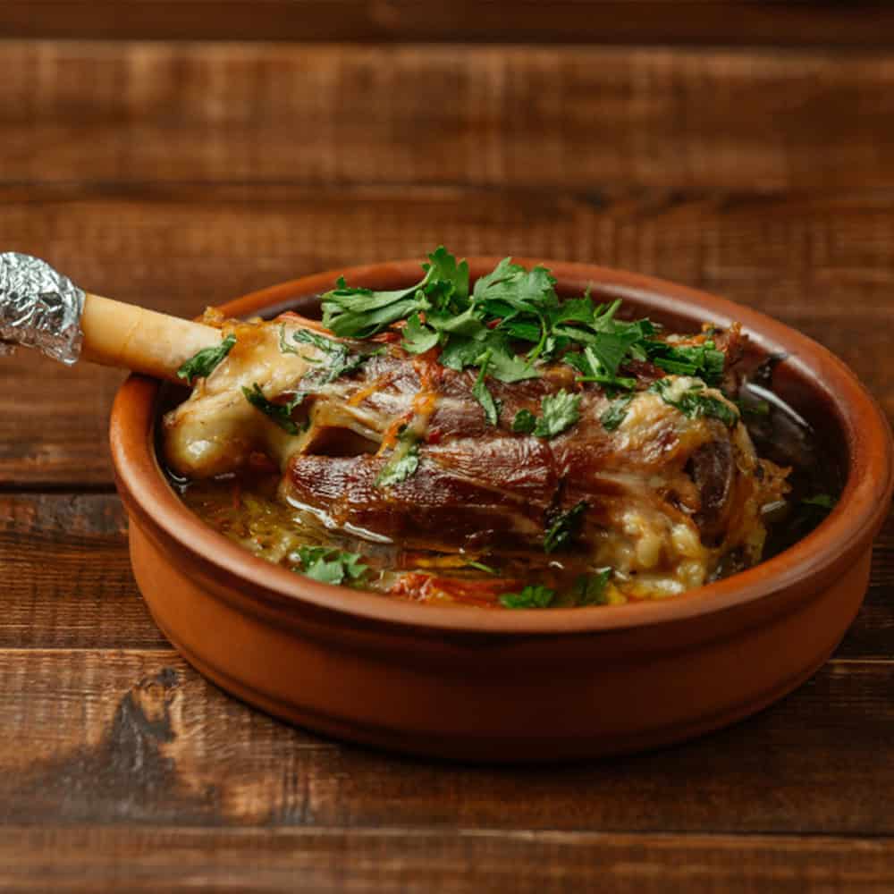 Savory Indian lamb curry in a clay pot, garnished with fresh herbs. Authentic Indian cuisine at Crown Indian Windang.