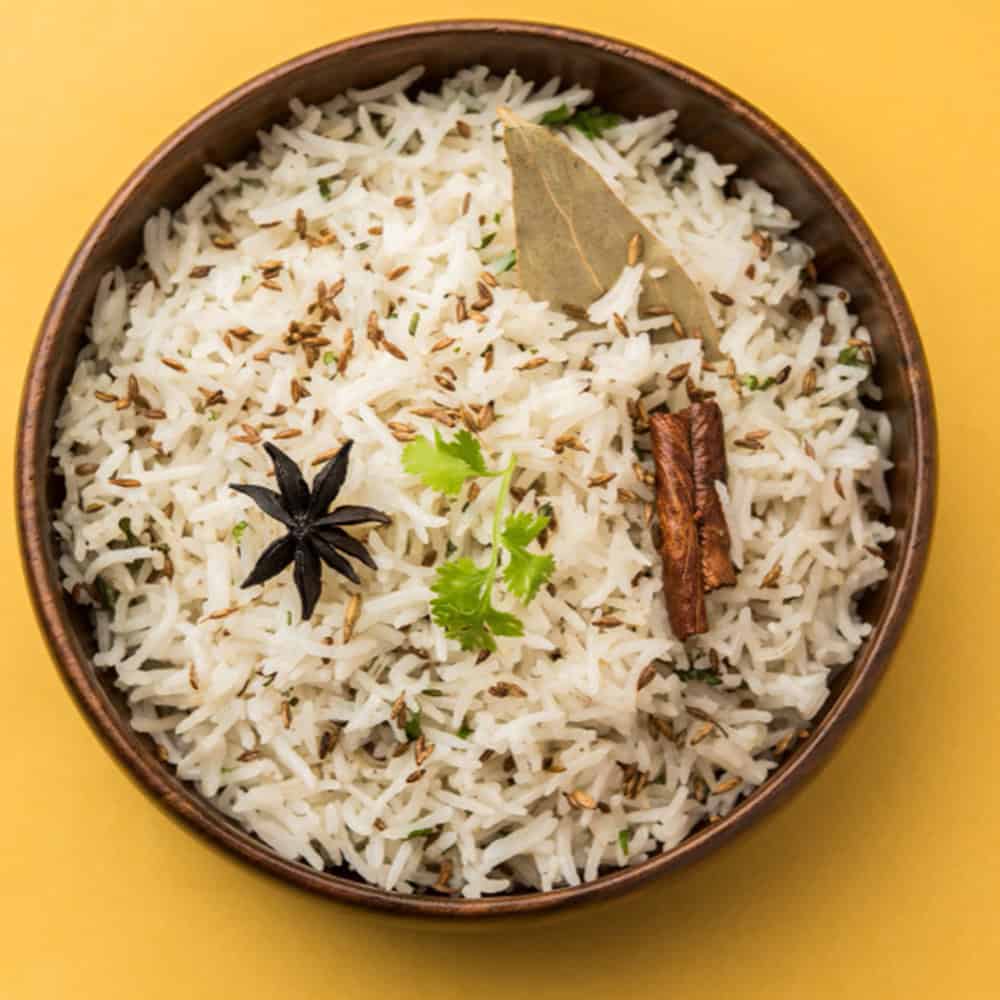 Fragrant basmati rice with Indian spices, herbs, and whole spices in a brown bowl on yellow background.