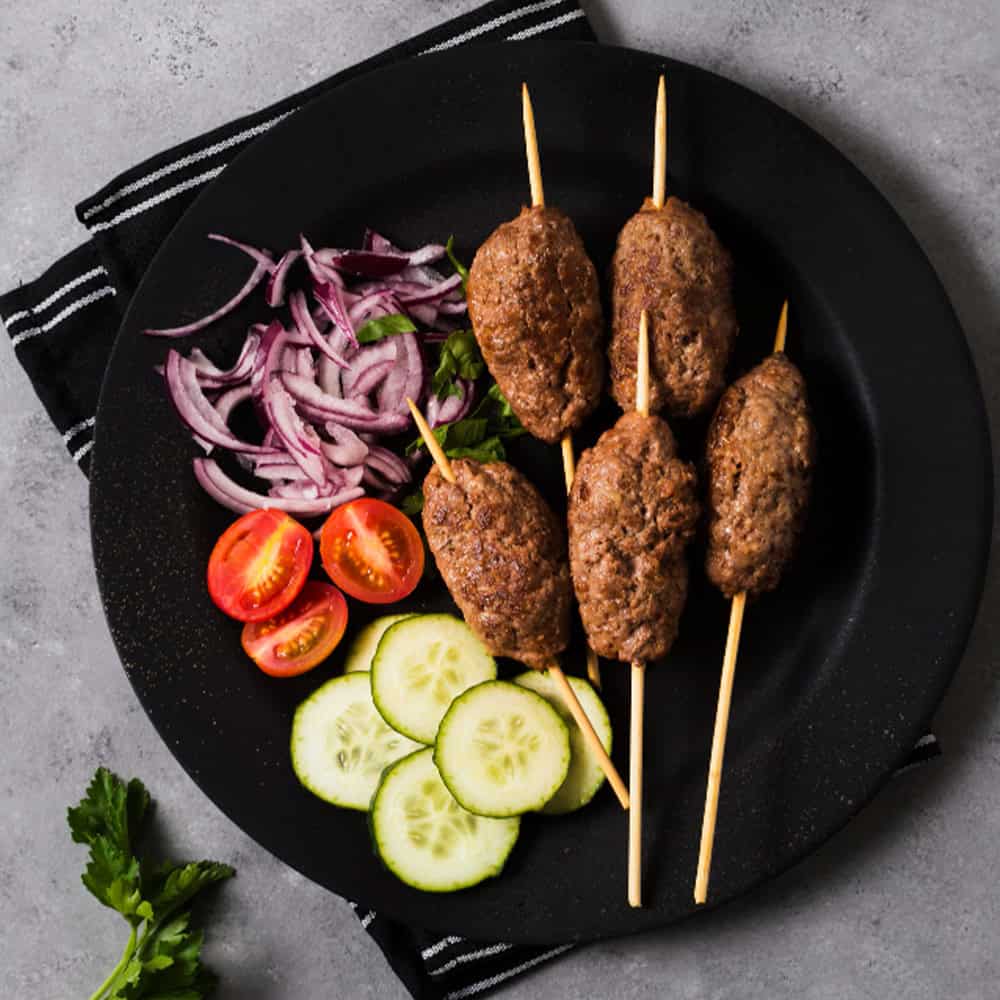 Delicious Indian kebabs with fresh vegetables on a black plate.