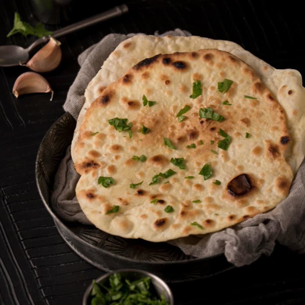 Soft Indian naan bread garnished with fresh herbs, cooked to golden perfection.