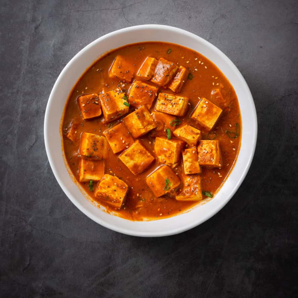 Spicy Indian paneer curry in a white bowl, close-up.