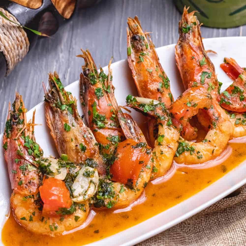 Juicy grilled prawns with herbs and spices on a white platter, served with flavorful sauce.