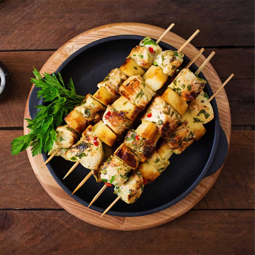 Skewers of grilled Indian chicken tikka with herbs and spices, served with fresh garnish.