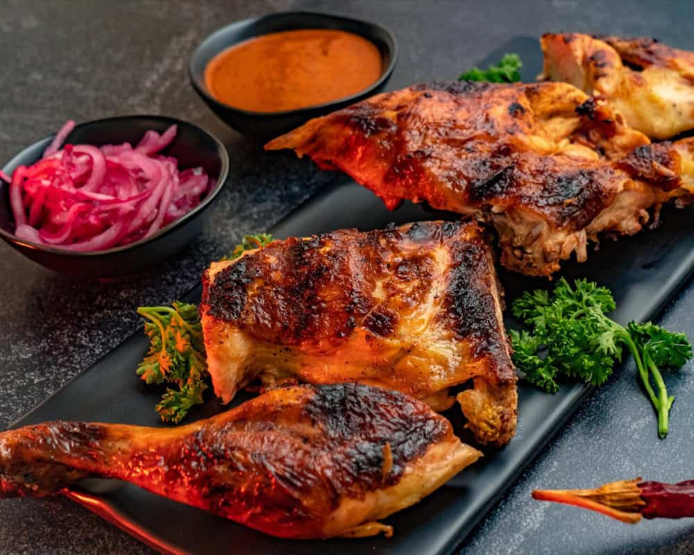 Juicy grilled chicken tikka with Indian spices on black platter, garnished with cilantro.
