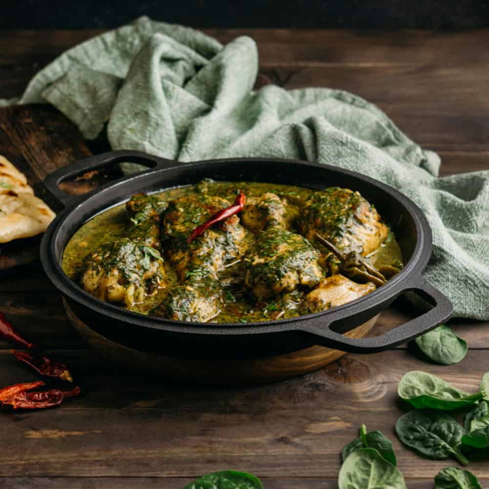 Spicy Indian chicken curry in a black cast iron dish with fresh spinach and herbs.