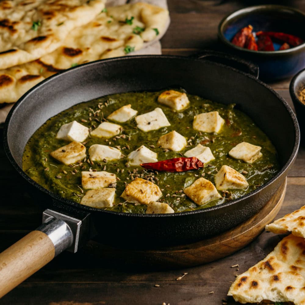 Spicy Indian vegetarian curry with paneer and herbs served in a black skillet.
