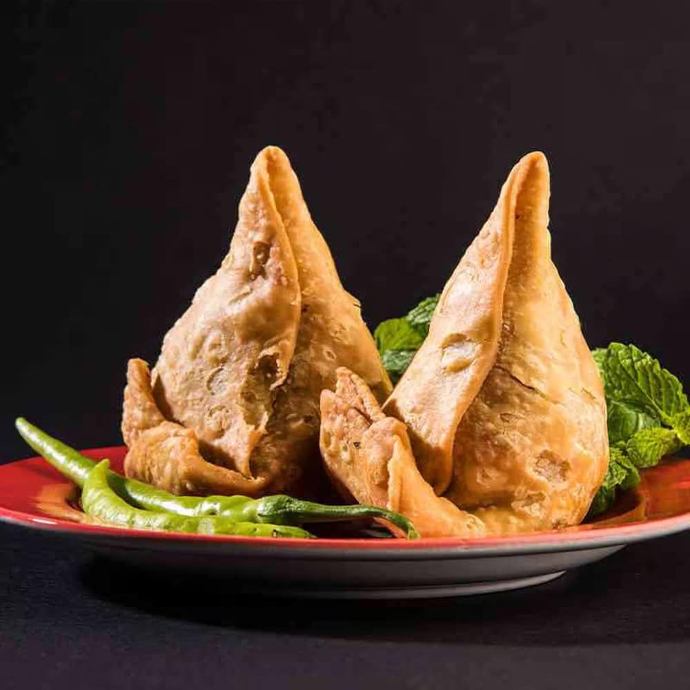 Crispy Indian samosas on a red plate with green chili peppers and mint leaves, served at Crown Indian Cuisine Windang.