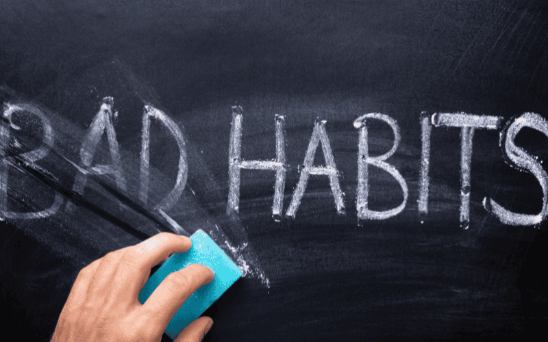 Hand erasing 'BAD HABITS' written on a blackboard with chalk.
