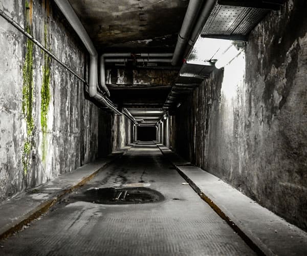 Dark underground tunnel with pipes and concrete walls for therapy space.