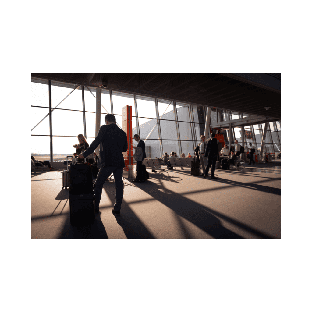 A business traveler pulling luggage at the airport terminal, with people waiting in the background.