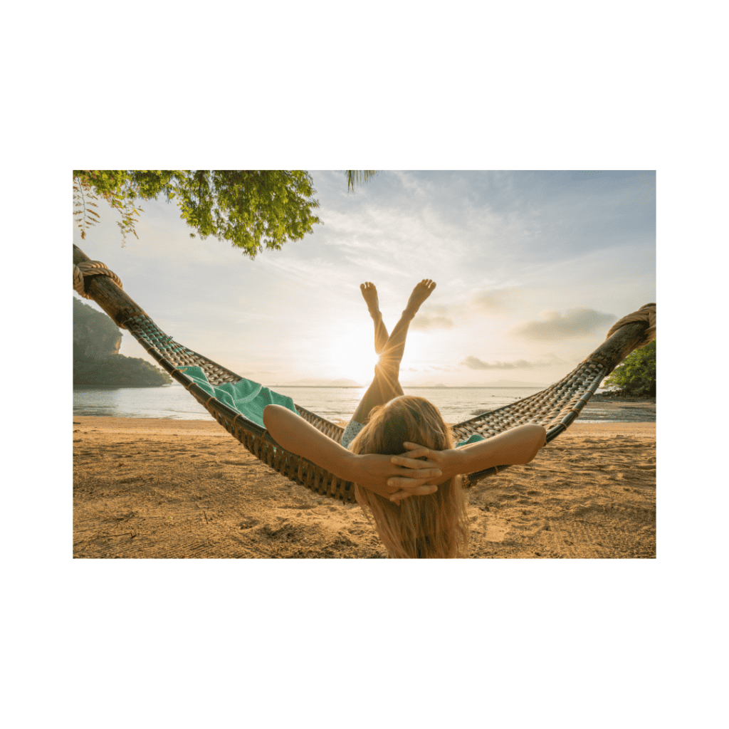 Woman relaxing in a hammock by the beach with the sun setting over the ocean.