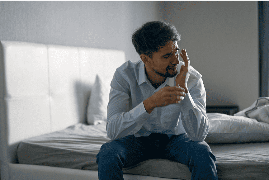 A man sitting on the edge of a bed, appearing upset and overwhelmed by PTSD symptoms.