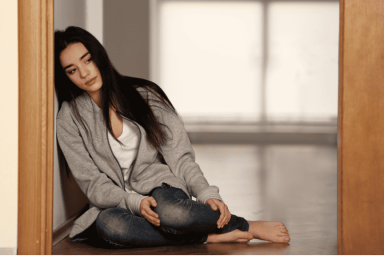 Young woman sitting on the floor, looking sad and lost in thought, symbolising depression and emotional struggles.