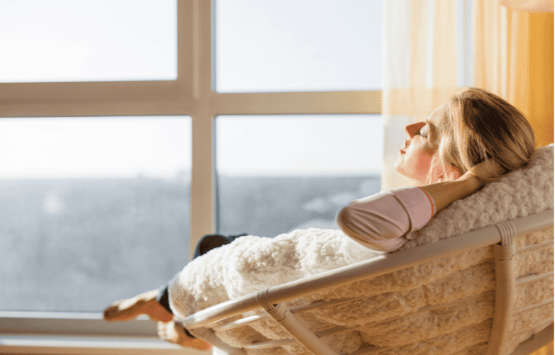Woman relaxing on a lounge chair by the window, enjoying sunlight and peace.