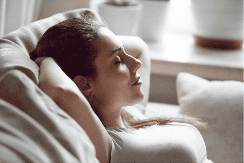 Woman relaxing on sofa during hypnotherapy session for stress relief.