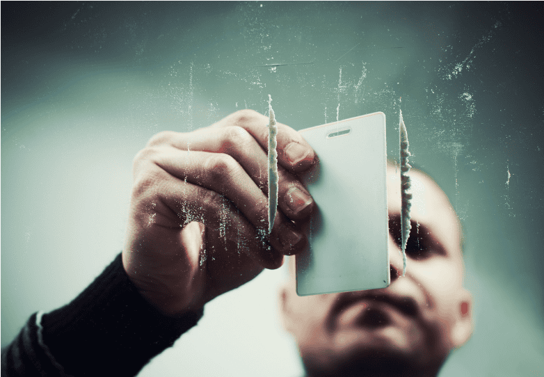 Man preparing lines of cocaine on a glass surface using a plastic card