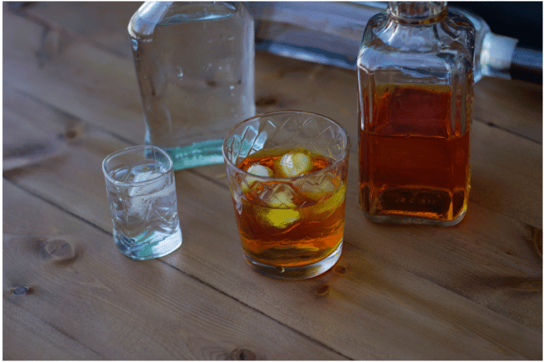 Whiskey and vodka in glass tumblers with bottles on a wooden table, symbolizing alcohol use and dependency.