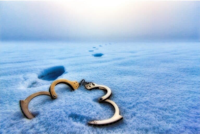 Broken handcuffs lying in snow with footprints leading into the distanc