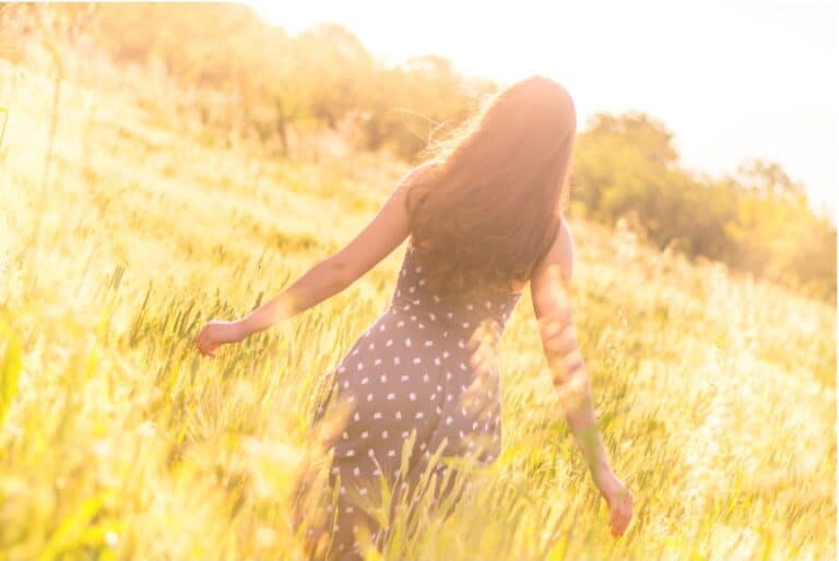 Woman walking peacefully through a sunlit field, embracing natural calm