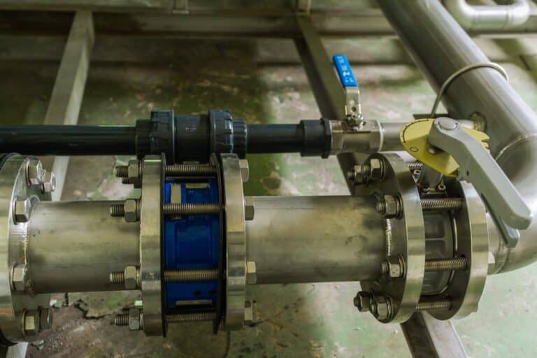 Close-up view of industrial metal piping with flanges, bolts, a blue valve section, and a lever handle valve in a facility—ideal for Backflow Testing and ensuring proper Backflow Prevention in Beltsville MD.