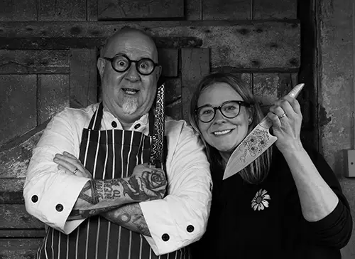 Nick & Daisy Kives Two chefs posing with knives in restaurant kitchen.