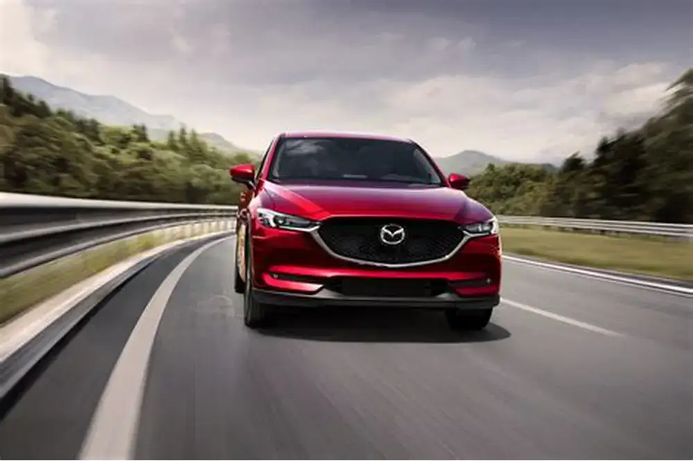 Red Mazda sedan driving on a scenic highway, showcasing sleek design and smooth performance, ideal for car enthusiasts and Mazda owners in Del Mar.