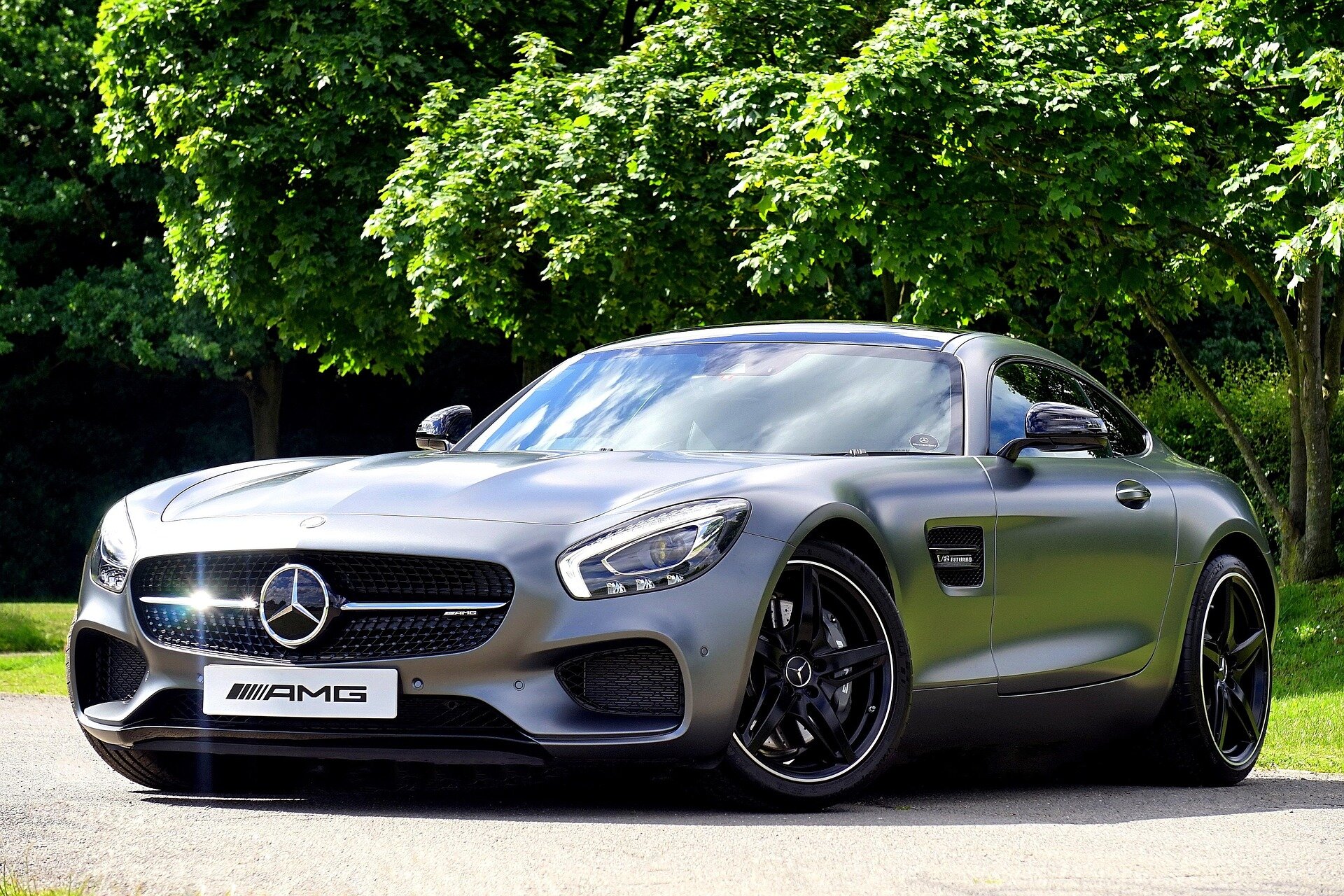 Silver Mercedes-Benz AMG convertible parked outdoors with lush green trees in the background, showcasing luxury and performance.