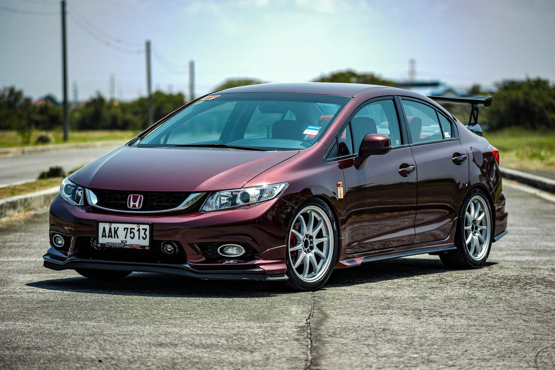 Customized Honda Civic sedan parked outdoors, showcasing aftermarket wheels, lowered suspension, and a rear spoiler for enhanced performance and style.